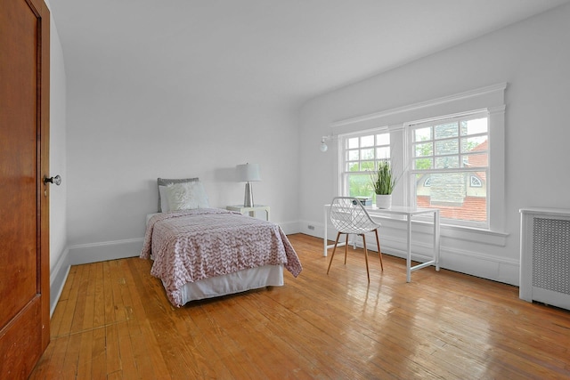bedroom with radiator heating unit, wood-type flooring, and baseboards