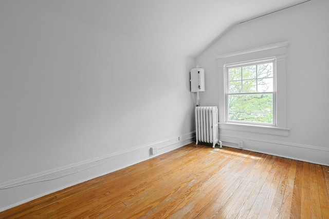 spare room featuring radiator, light wood-type flooring, and lofted ceiling