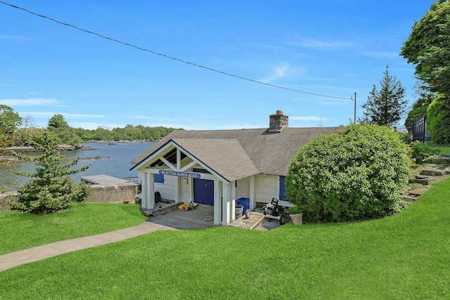 rear view of house featuring a shingled roof, a yard, a water view, and a chimney