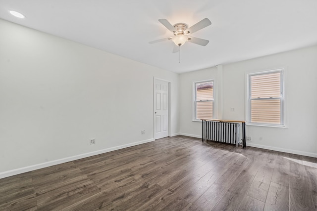 empty room featuring radiator, ceiling fan, baseboards, and dark wood-style flooring
