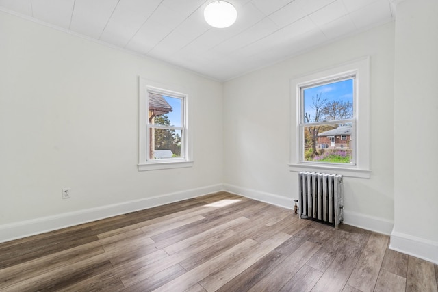 unfurnished room with baseboards, ornamental molding, wood finished floors, and radiator