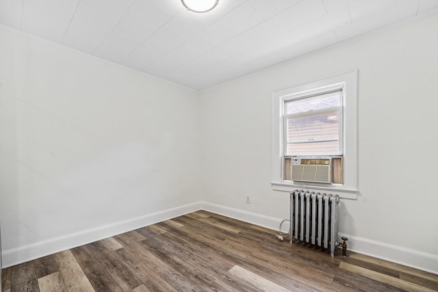 empty room with crown molding, cooling unit, radiator heating unit, baseboards, and wood finished floors