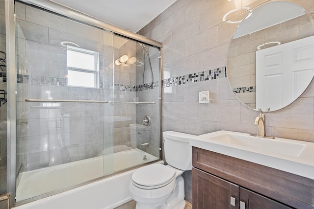 full bath featuring toilet, tile walls, combined bath / shower with glass door, and vanity