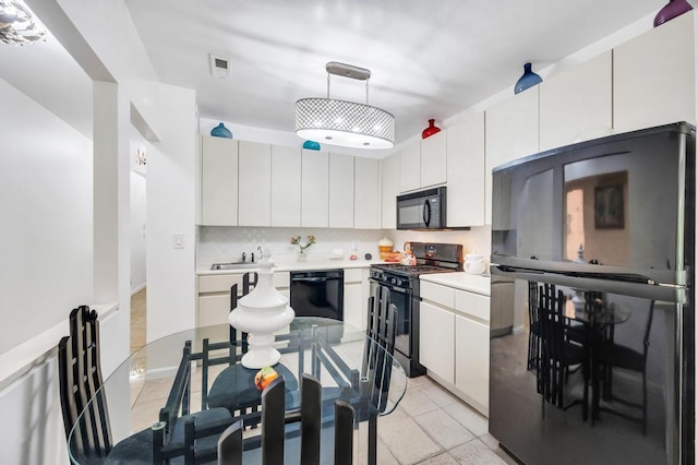 kitchen with light countertops, white cabinets, backsplash, black appliances, and hanging light fixtures