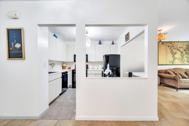 kitchen with tasteful backsplash, light countertops, baseboards, black appliances, and white cabinetry