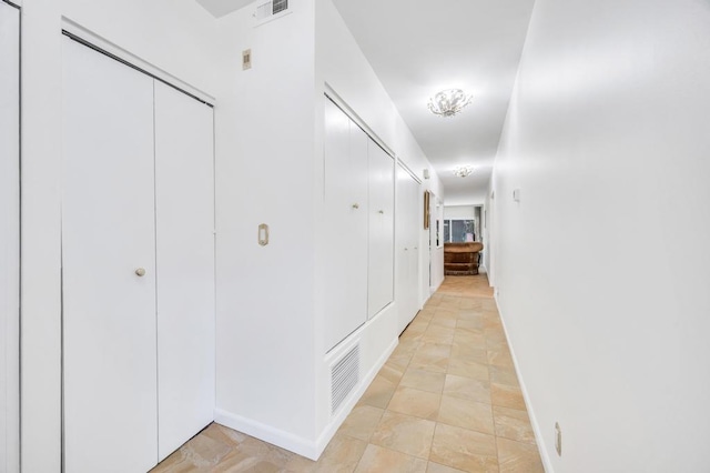 hallway with baseboards, stone finish floor, and visible vents