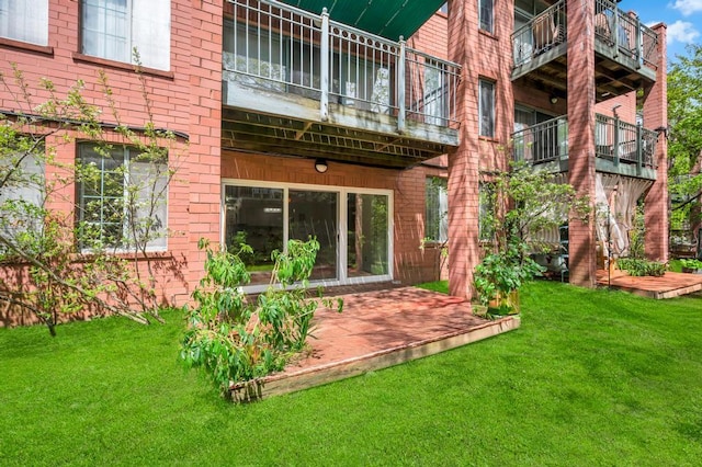 rear view of house with brick siding, a balcony, and a yard