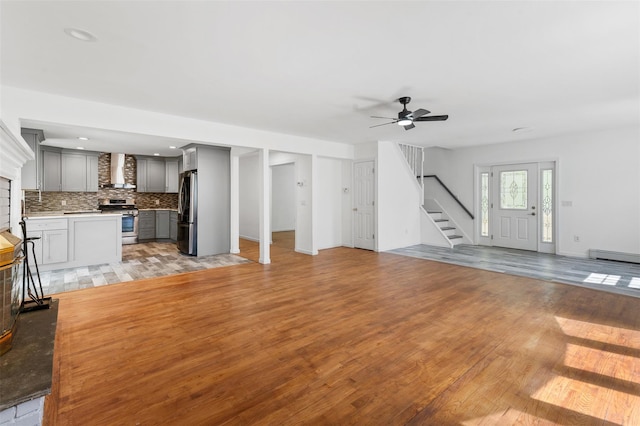 unfurnished living room with baseboard heating, stairs, a ceiling fan, recessed lighting, and light wood-type flooring