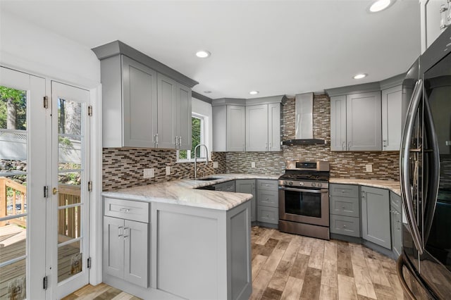 kitchen with a sink, stainless steel gas stove, wall chimney exhaust hood, refrigerator, and gray cabinetry