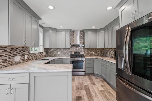 kitchen featuring wall chimney range hood, light stone counters, a sink, stainless steel appliances, and gray cabinetry