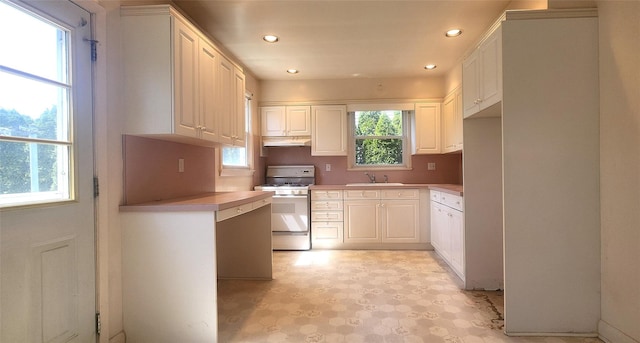 kitchen featuring white gas range oven, a sink, recessed lighting, under cabinet range hood, and white cabinets