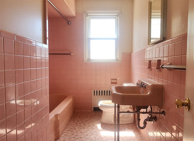 bathroom with radiator, tile walls, a tub to relax in, toilet, and wainscoting