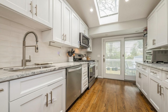 kitchen featuring white cabinetry, a sink, appliances with stainless steel finishes, backsplash, and a skylight