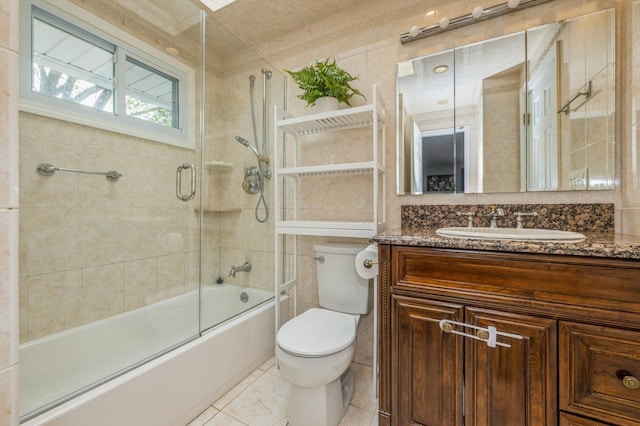 bathroom featuring combined bath / shower with glass door, tile walls, vanity, and toilet