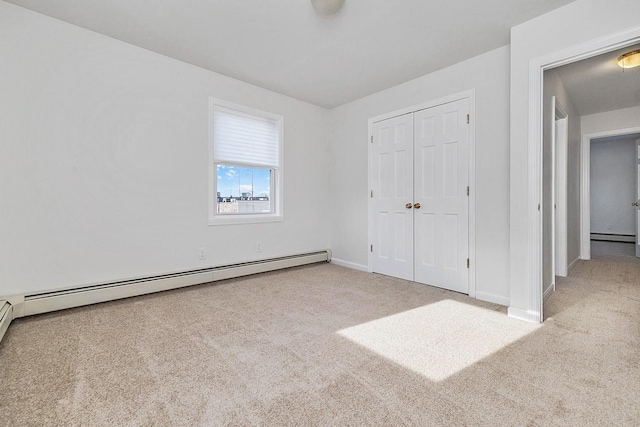 unfurnished bedroom with carpet floors, a baseboard radiator, baseboards, and a closet