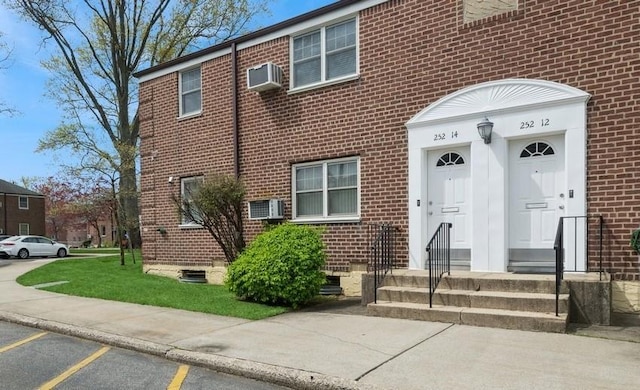 view of front of house with an AC wall unit, uncovered parking, and brick siding