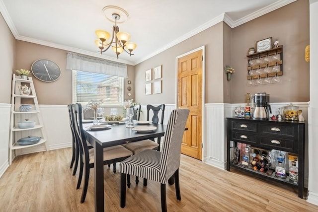 dining space featuring an inviting chandelier, ornamental molding, light wood-style floors, and wainscoting