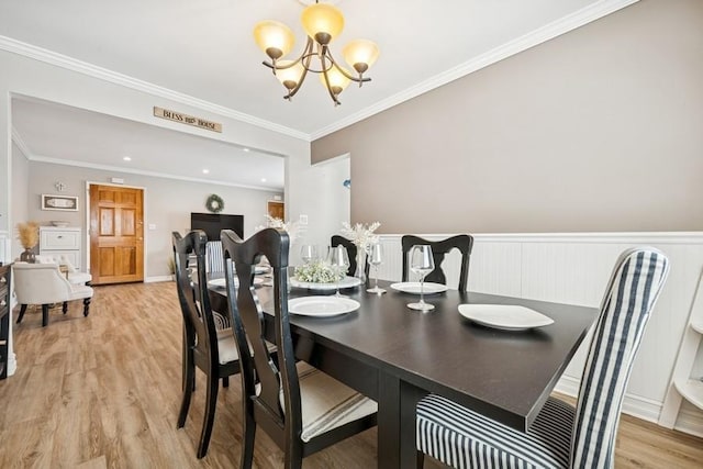 dining area featuring light wood-style floors, a wainscoted wall, ornamental molding, and a chandelier