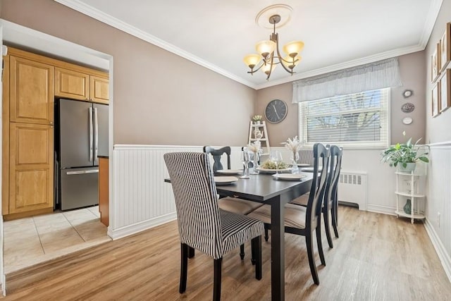 dining room featuring wainscoting, a chandelier, ornamental molding, and light wood-type flooring