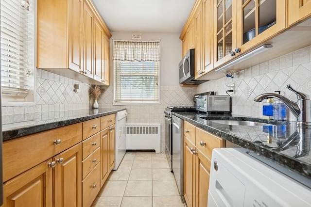 kitchen featuring appliances with stainless steel finishes, a sink, dark stone countertops, radiator, and light tile patterned flooring