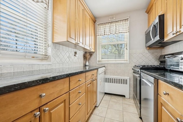 kitchen featuring dark stone countertops, appliances with stainless steel finishes, radiator heating unit, and light tile patterned floors
