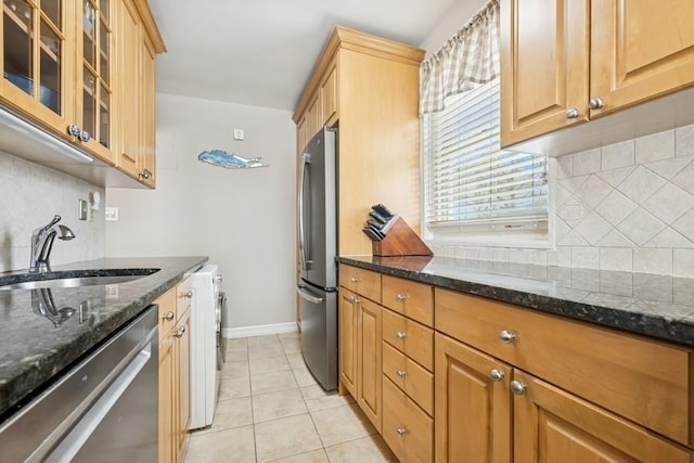 kitchen with a sink, dark stone counters, appliances with stainless steel finishes, and tasteful backsplash