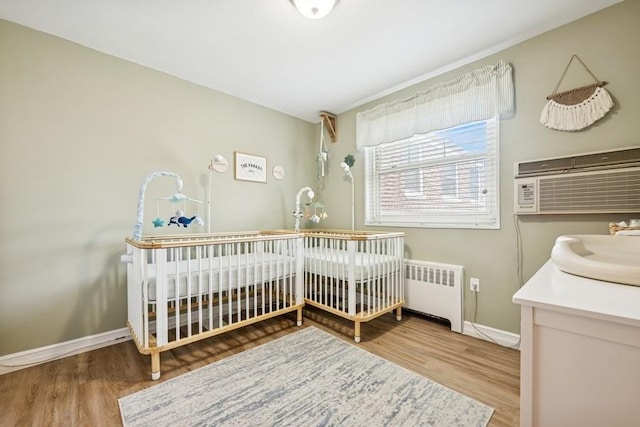 bedroom featuring a nursery area, baseboards, wood finished floors, and radiator