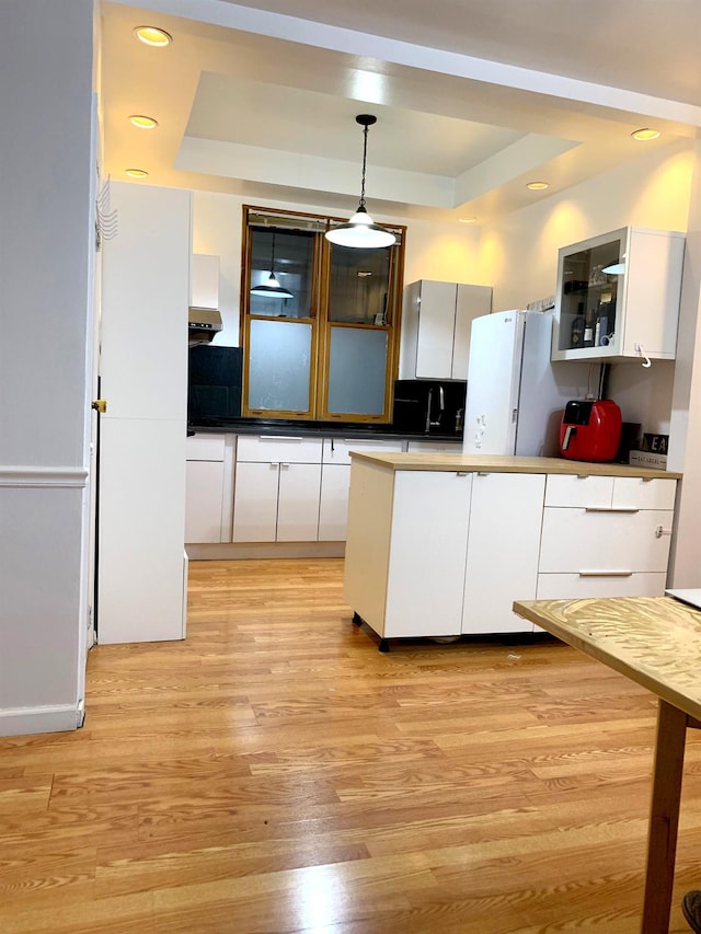 kitchen featuring freestanding refrigerator, white cabinetry, and a tray ceiling