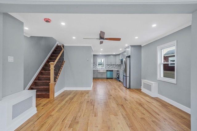 unfurnished living room with crown molding, ceiling fan, light wood finished floors, stairs, and baseboards