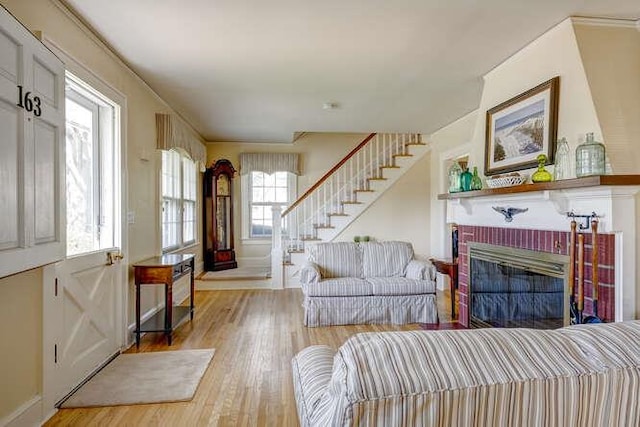 living room featuring baseboards, light wood finished floors, a brick fireplace, and stairs