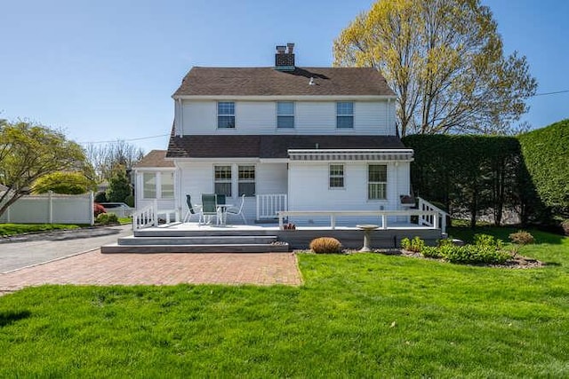 rear view of property featuring a lawn, fence, a chimney, and a deck