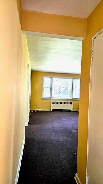 spare room with radiator, baseboards, and dark carpet