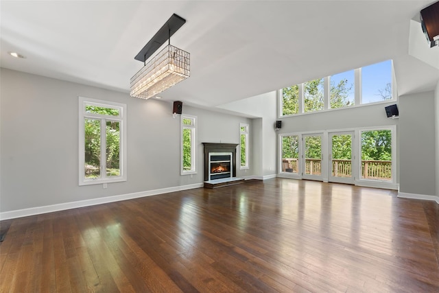 unfurnished living room with baseboards, wood-type flooring, a glass covered fireplace, and a high ceiling