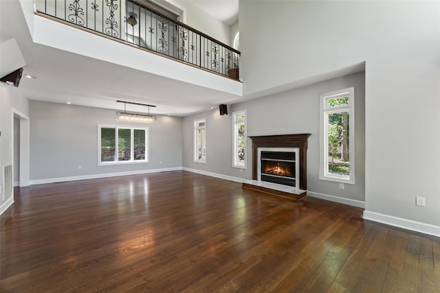 unfurnished living room featuring a glass covered fireplace, baseboards, a high ceiling, and wood-type flooring