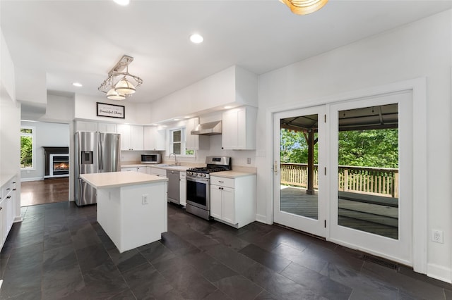 kitchen with appliances with stainless steel finishes, wall chimney exhaust hood, a sink, light countertops, and white cabinetry