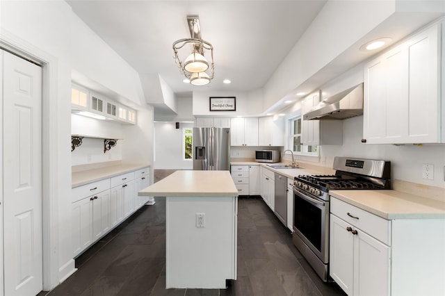 kitchen featuring a kitchen island, wall chimney exhaust hood, white cabinetry, a sink, and appliances with stainless steel finishes
