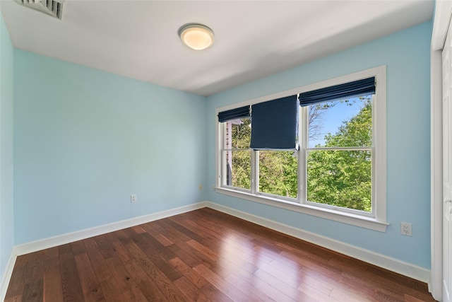 empty room with baseboards, visible vents, and dark wood-style floors