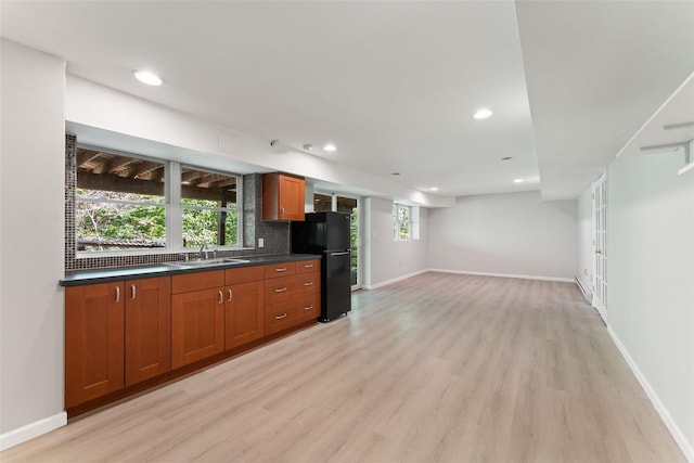 kitchen featuring dark countertops, a sink, freestanding refrigerator, baseboards, and light wood-type flooring