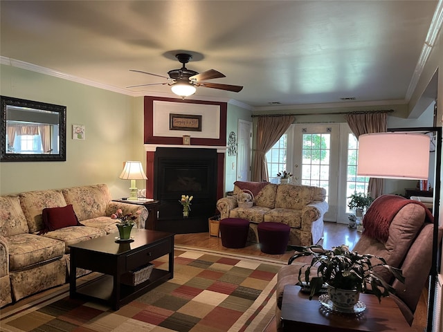 living area with a ceiling fan, wood finished floors, a fireplace, and ornamental molding