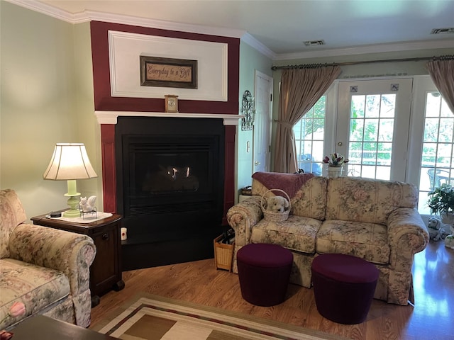 living area featuring a fireplace with flush hearth, visible vents, ornamental molding, and wood finished floors