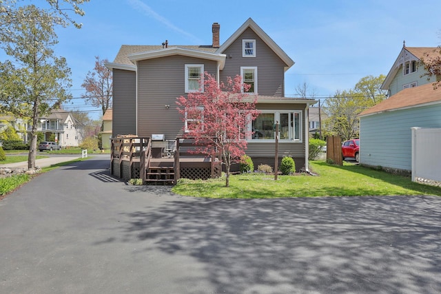 rear view of property featuring a chimney, a lawn, and a deck