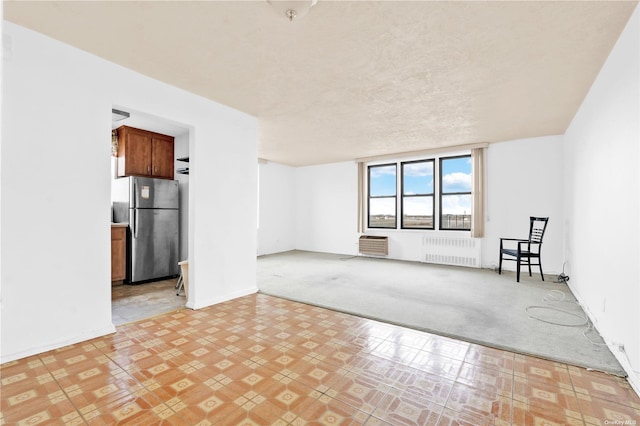 spare room featuring light colored carpet, a textured ceiling, baseboards, and radiator heating unit