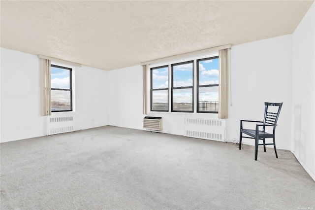 spare room featuring carpet floors, a textured ceiling, a wall unit AC, and radiator