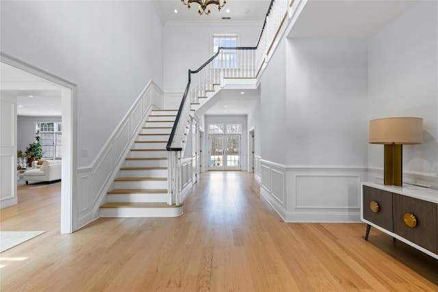 entryway featuring light wood-type flooring, stairway, a decorative wall, and a high ceiling