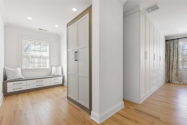hallway with light wood-type flooring, baseboards, crown molding, and visible vents
