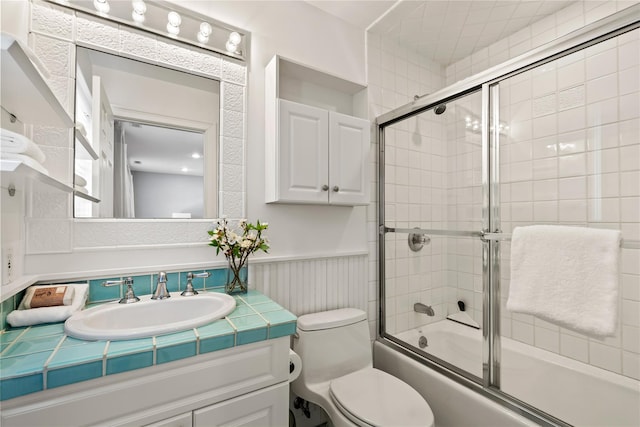 bathroom featuring toilet, wainscoting, vanity, and combined bath / shower with glass door