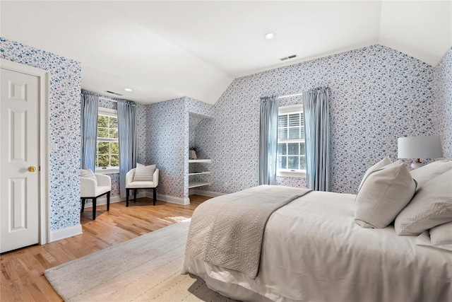 bedroom featuring wood finished floors, wallpapered walls, visible vents, baseboards, and lofted ceiling