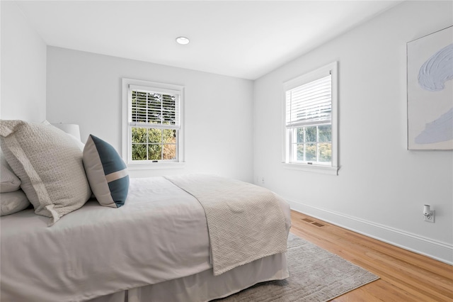bedroom with baseboards, multiple windows, visible vents, and wood finished floors
