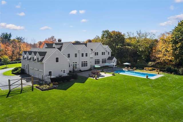 back of property featuring fence, an outdoor pool, a garage, a patio, and a lawn