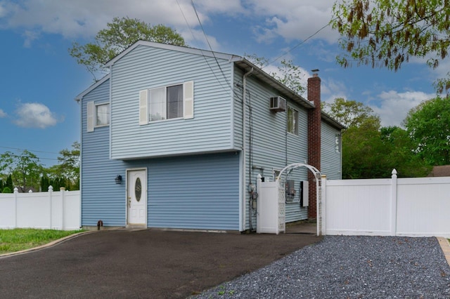 view of side of property featuring fence, a chimney, driveway, and a wall mounted AC
